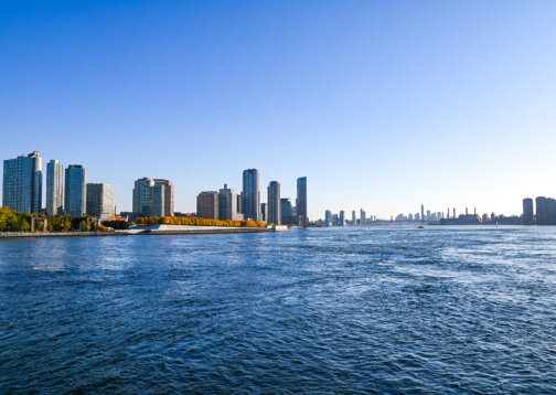 A view of the New York skyline from across the Hudson River on a clear, sunny day.