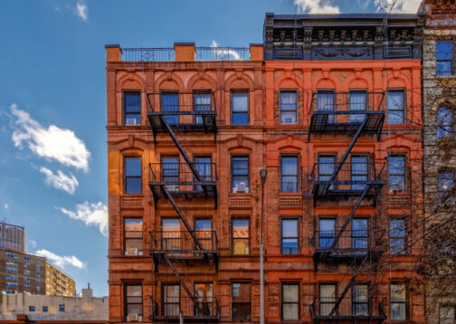 A classic red brick apartment building in New York City with black fire escapes on the front.