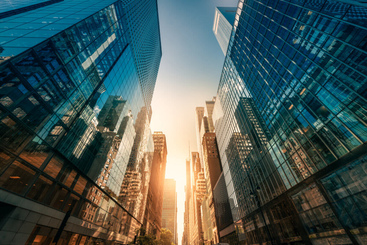 A worm's eye view of tall buildings with glass facade reflecting the blue sky, creating a modern urban landscape.