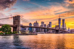 New York City Skyline with the sunset reflecting on the East River and views of the Brooklyn Bridge.