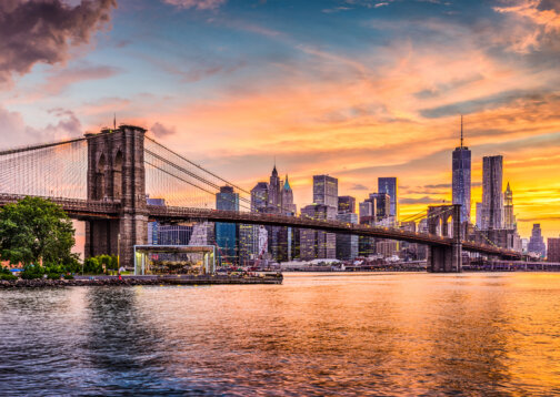 New York City Skyline with the sunset reflecting on the East River and views of the Brooklyn Bridge.
